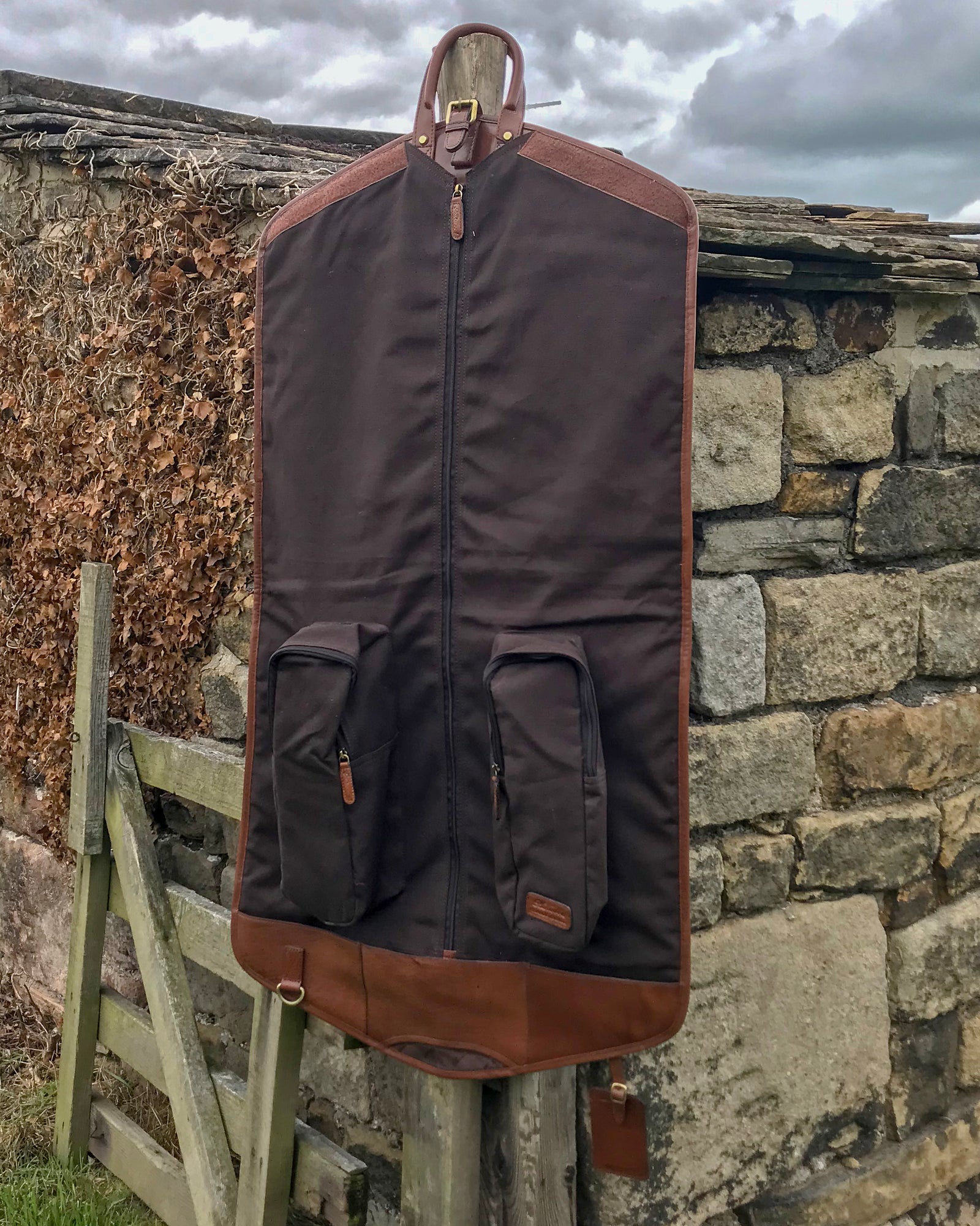 Ashwood chestnut leather Suit Carrier hung up open against stone wall