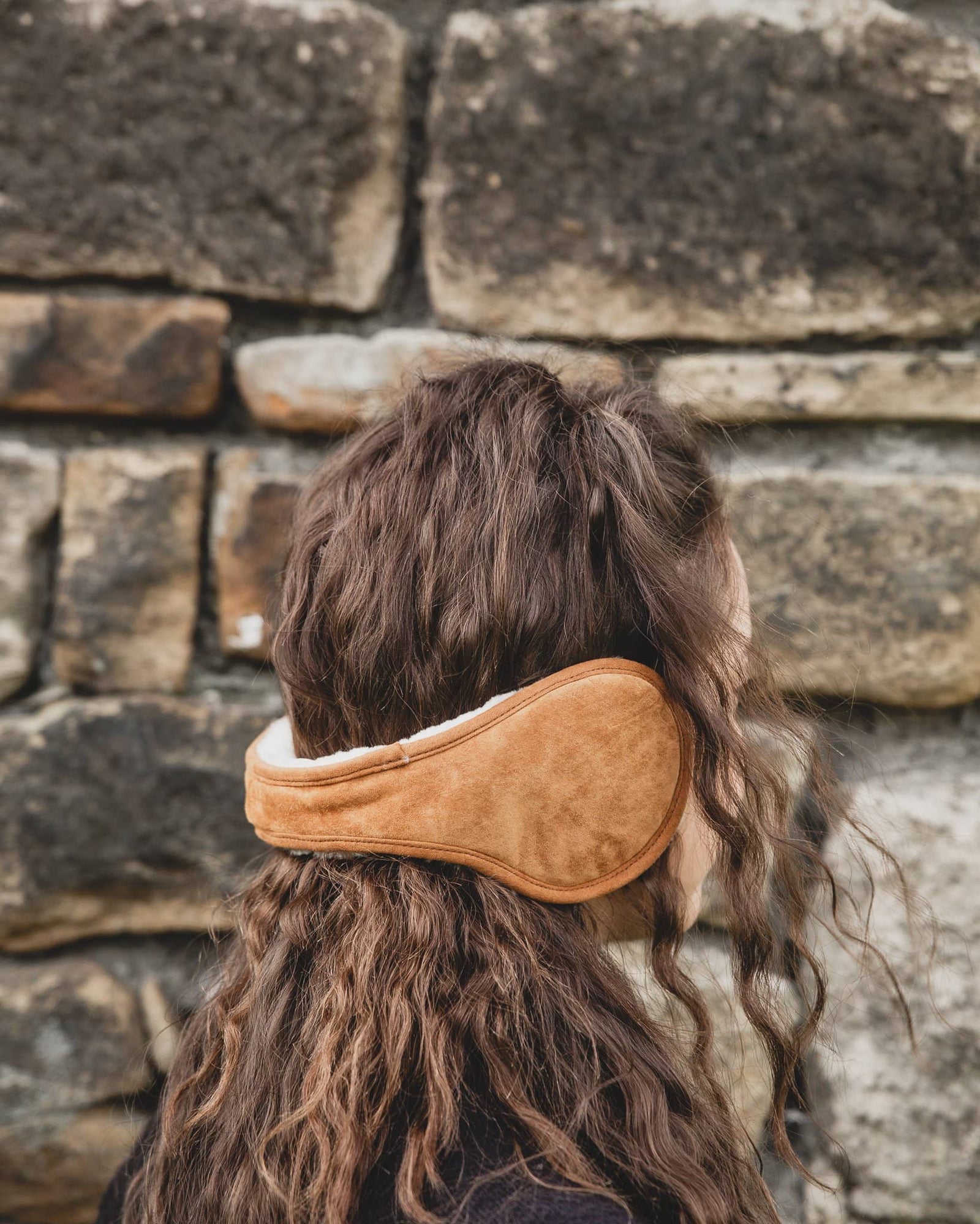 Nordvek adults sheepskin earmuffs 513-100 chocolate model wearing in front of stone wall